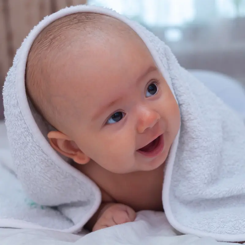 Happy baby wrapped in a soft white towel after bath time